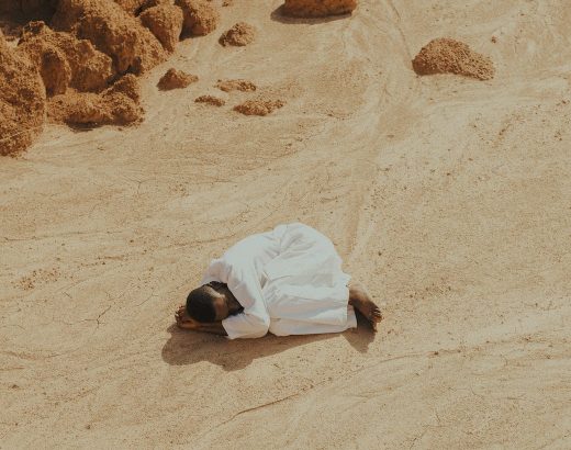 man dressed in white lying curled up on a desert
