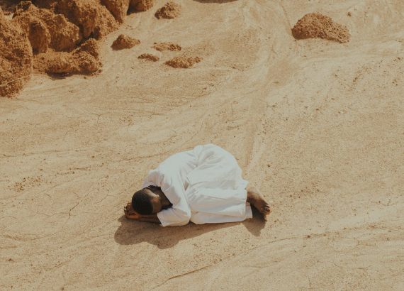 man dressed in white lying curled up on a desert