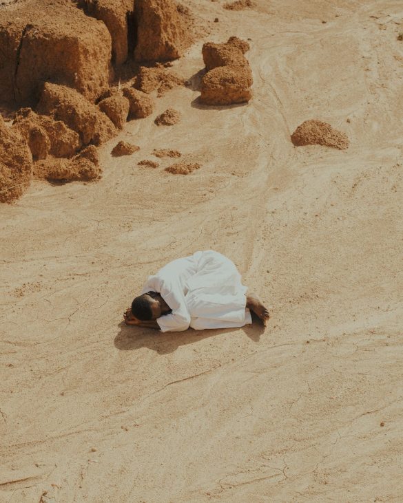 man dressed in white lying curled up on a desert