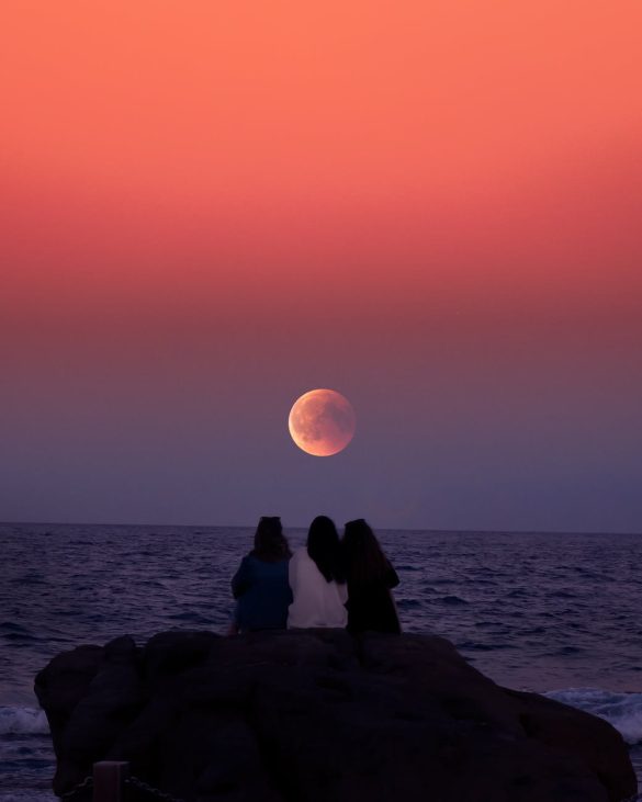 women sitting on rock infront of ocean